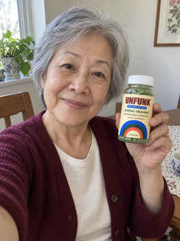 Woman in a burgundy top holding UNFUNK, in her dining nook