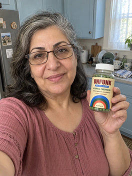 Woman in a dusty rose top holding UNFUNK, in her kitchen