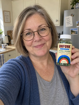 Woman in a blue cardigan holding UNFUNK, in her kitchen