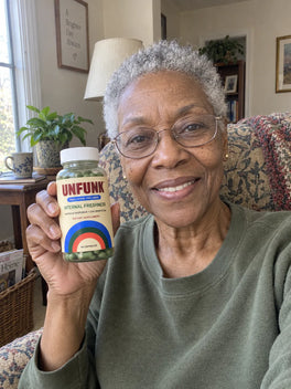 Woman in an olive sweatshirt holding UNFUNK, in her sitting room