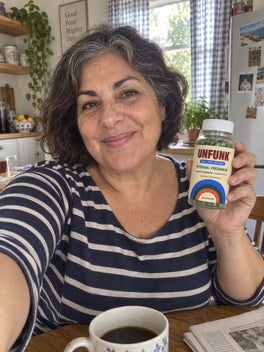 Woman in a navy striped top holding UNFUNK, in her breakfast nook
