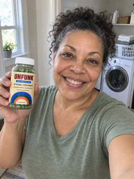 Woman in a sage top holding UNFUNK, in her laundry room