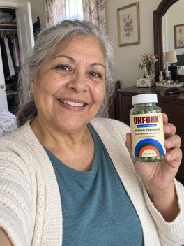 Woman in a cream cardigan holding UNFUNK, in her bedroom